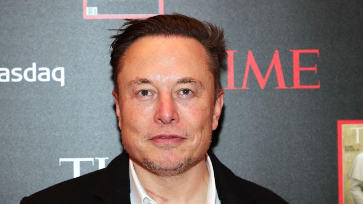 A close-up photograph of Elon Musk in front of a backdrop displaying the words 'Nasdaq' and 'TIME'