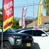 Used car lot with signs that read “drive out,” sale,” and “welcome”